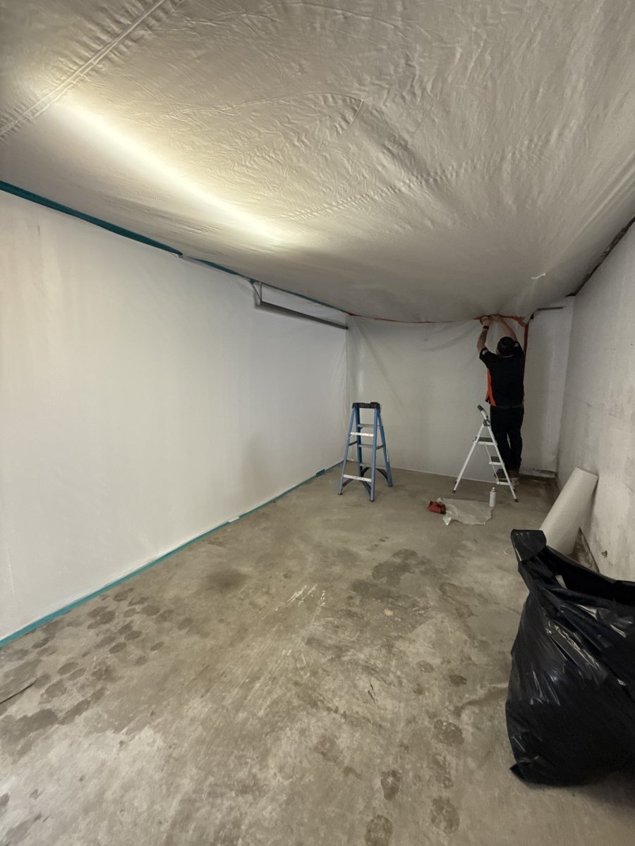 Full plastic containment with negative air set up during mold remediation - technician sealing the ceiling line