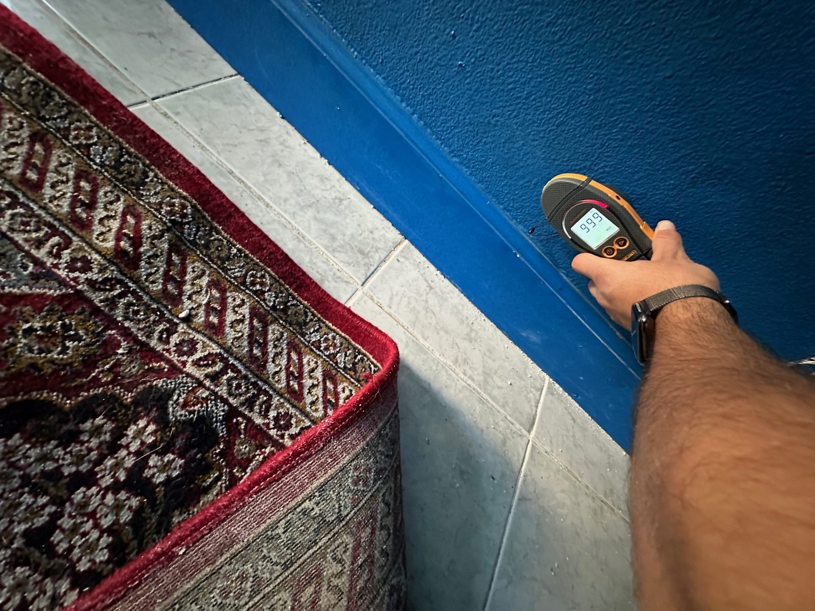 Instant Restoration job photo in Glendale, CA: Moisture meter held to baseboard beside rug; hand only, no face